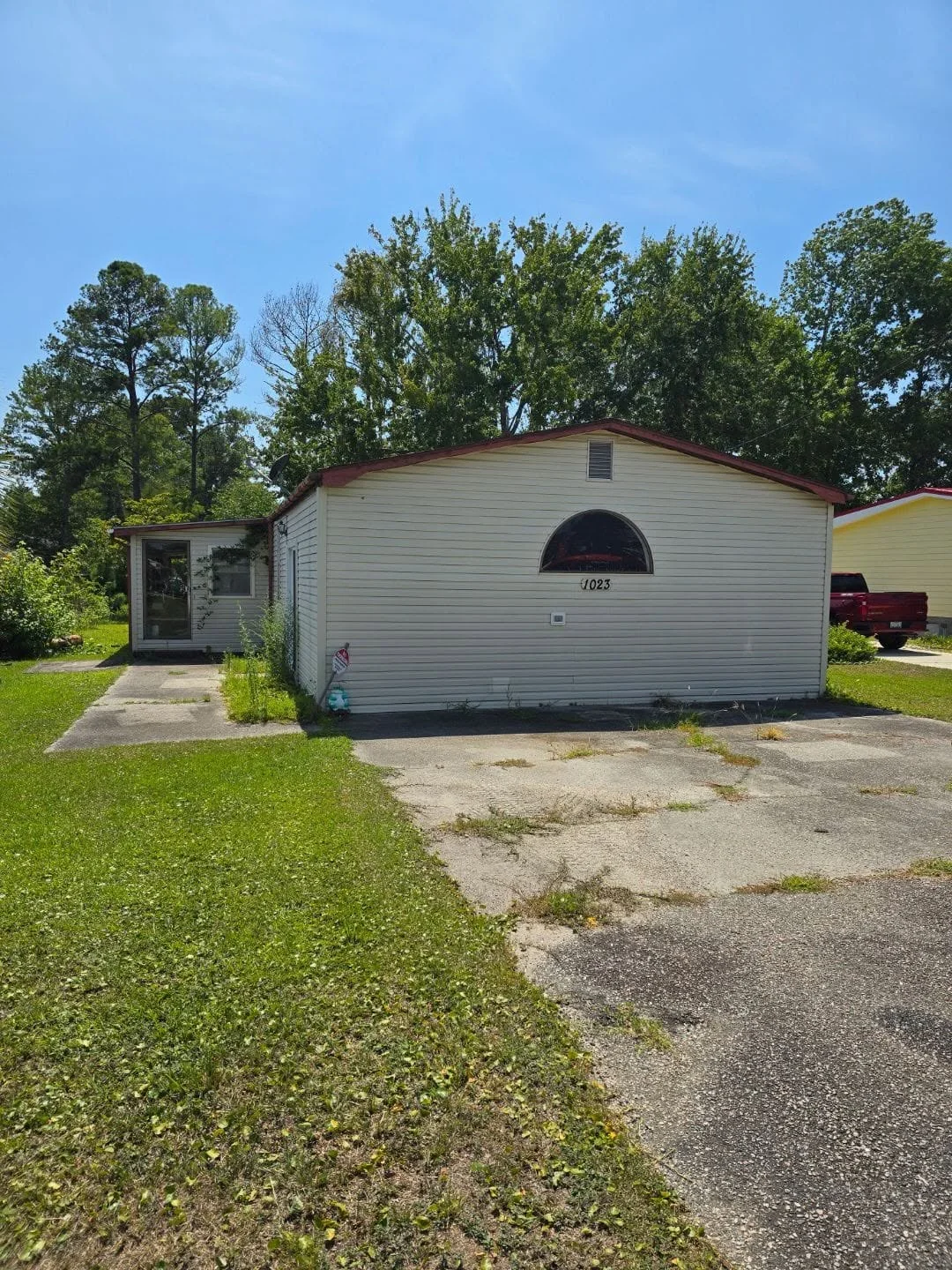 Single-wide mobile home with white vinyl siding and burgundy metal roof before demolition